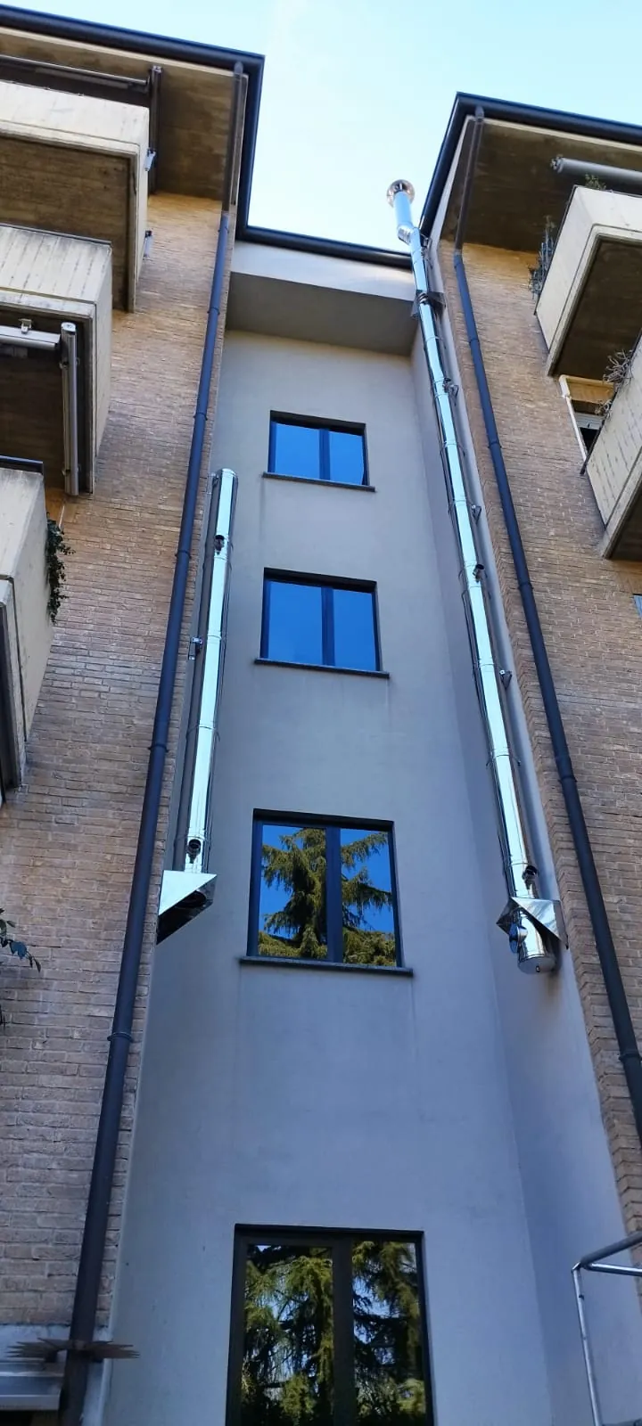 Due canne fumarie in acciaio inox installate in facciata su un condominio in mattoni