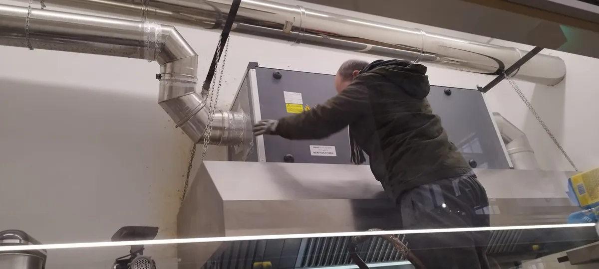 Tecnico al lavoro sull'unità filtrante montata sopra la cappa di una cucina professionale