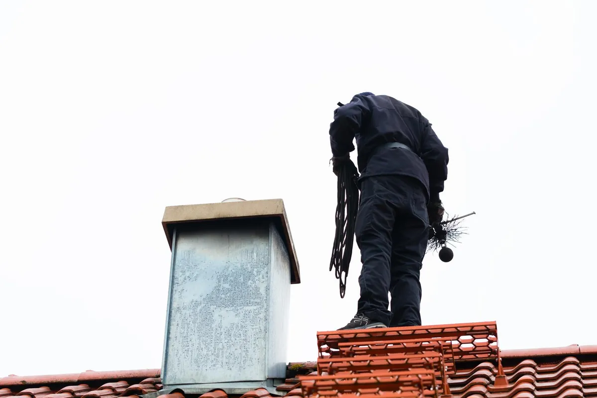 Spazzacamino sul tetto accanto al comignolo con corda e scovolo